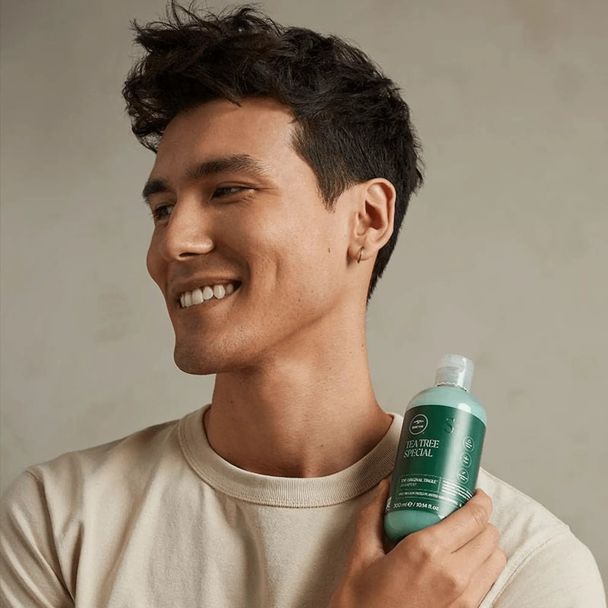 Homme Souriant tient une bouteille verte et blanche de Paul Mitchell Shampoing Tea Tree Special, 1L