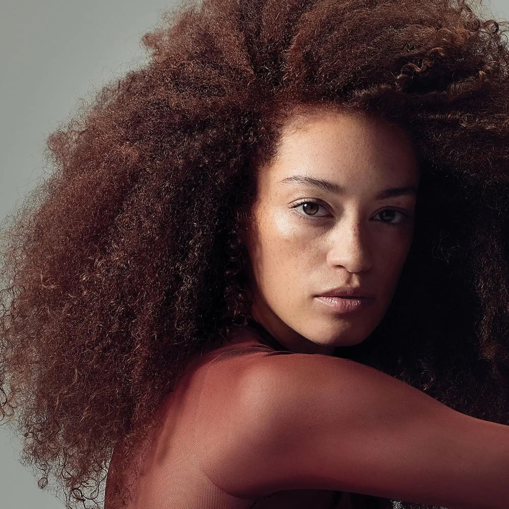 Femme après avoir utilisé le produit Paul Mitchell Twirl Around 150ml : beige et blanc pour cheveux ondulés et bouclés, offrant un contrôle des frisottis et une tenue douce et modulable.