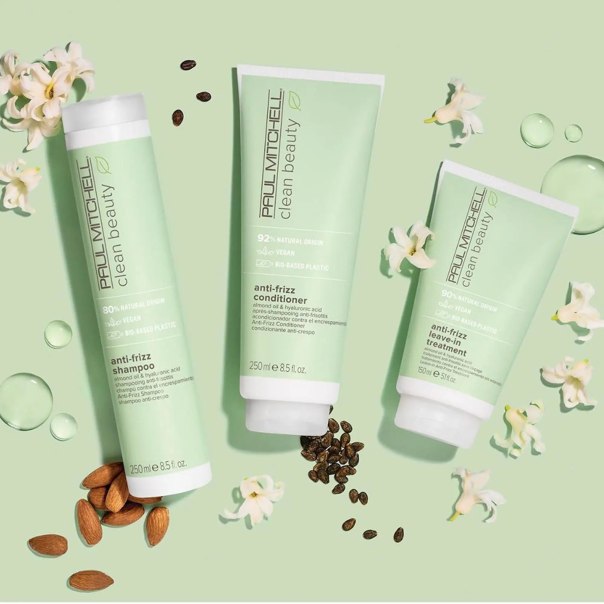 Tube de 250 ml et de 150ml du shampooing et du revitalisant anti-frisottis Paul Mitchell Clean Beauty vert pâle entouré d'amandes et de fleurs blanches sur fond vert pastel.