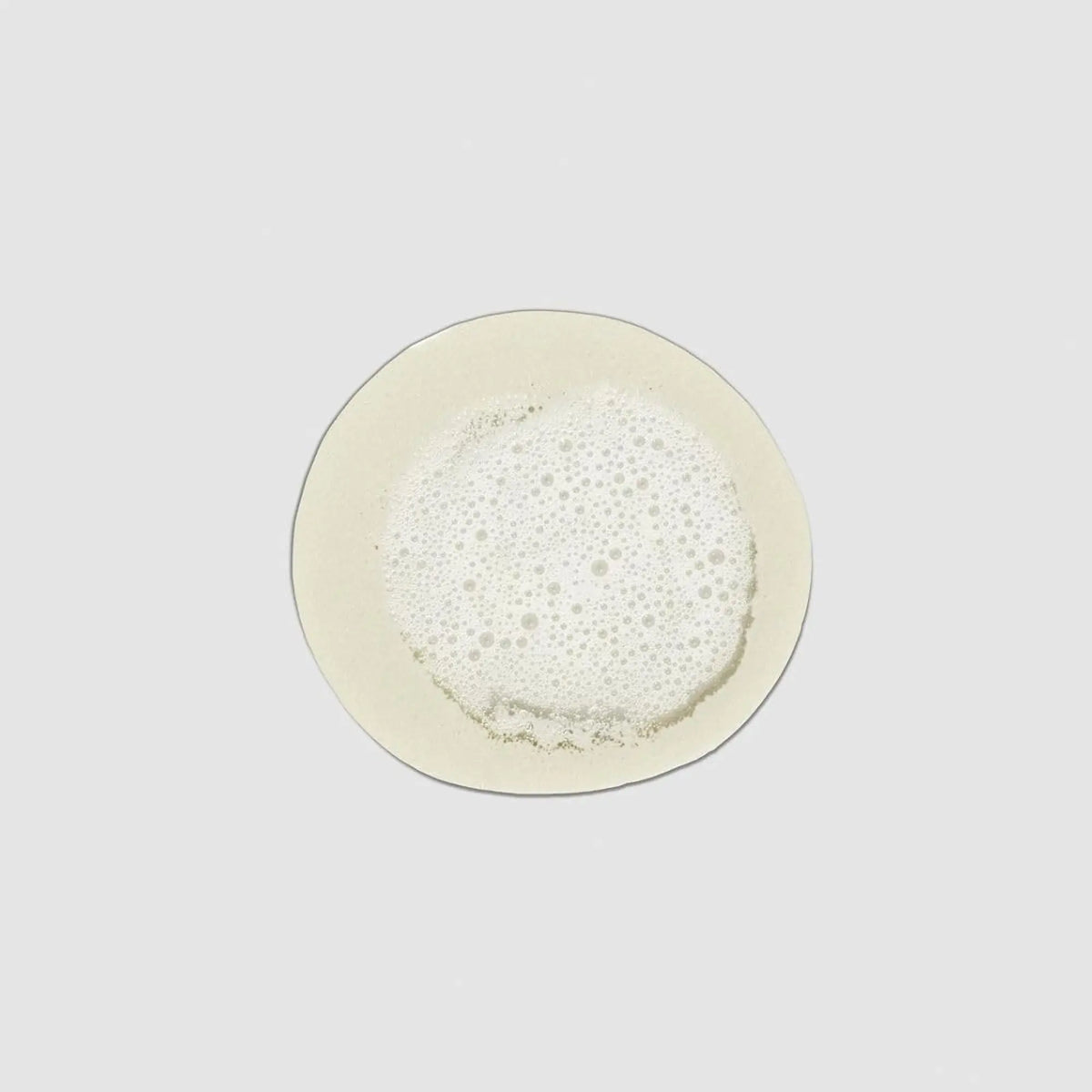 Échantillon de texture crémeuse et moussante du shampooing anti-frisottis Paul Mitchell Clean Beauty sur fond gris clair, montrant la consistance riche et légère du produit.